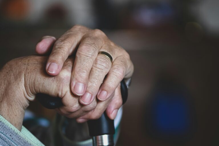 An elderly patient with their hands on a cane