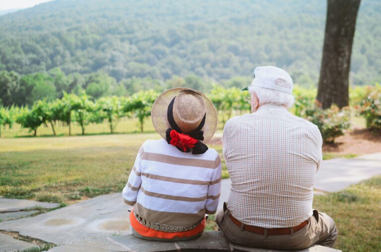 Two older individuals sitting on a bench outside during Summer